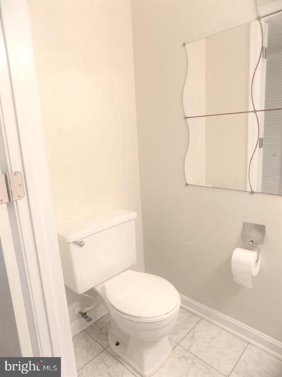 Small bathroom with a white toilet, large wall mirror, and marble-look tile floor.