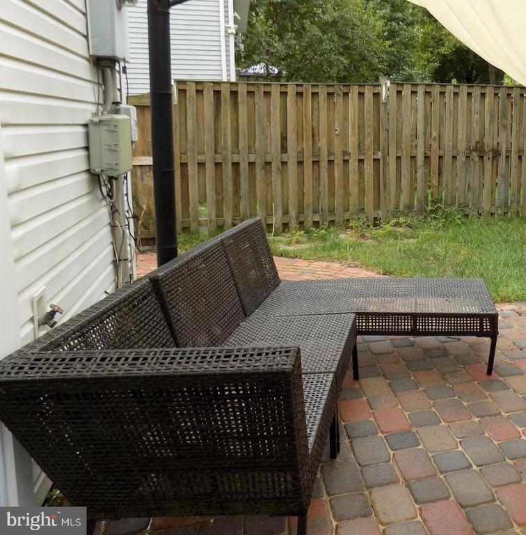 Backyard patio with a dark woven sectional, paver flooring, and a wooden privacy fence.