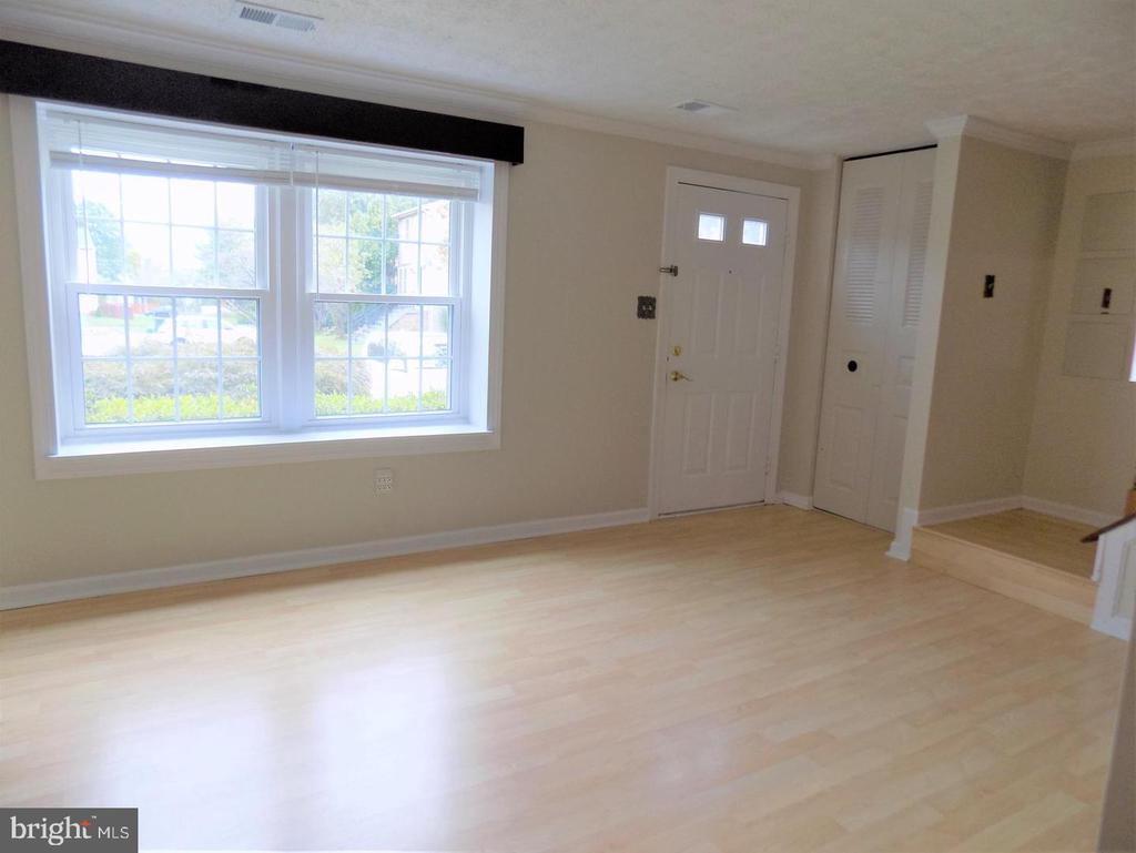 Empty entry room with light wood flooring, a large window, and a white front door.