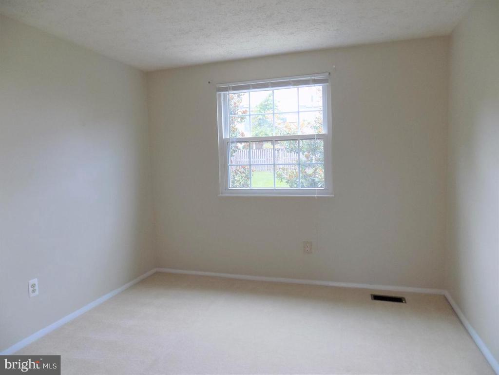 Empty carpeted room with neutral walls and a window overlooking a fenced, green yard.