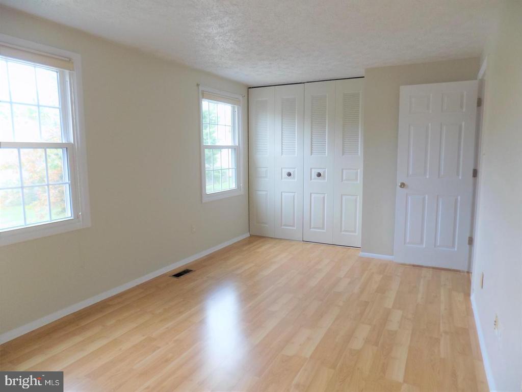 Vacant bedroom with light hardwood floors, two windows, and white closet doors.
