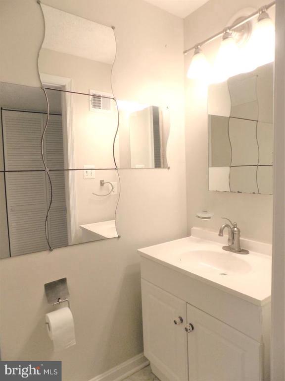 Bathroom with a white vanity, chrome faucet, mirrored walls, and bright vanity lights.