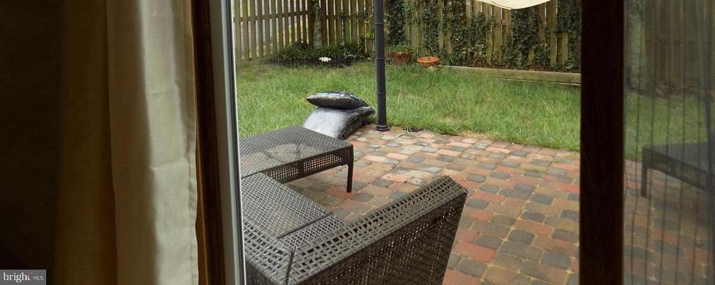 Brick paver patio with woven outdoor seating beside a fenced grassy backyard.