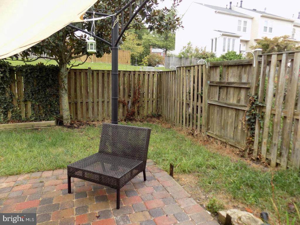 Fenced backyard patio with a woven chair, umbrella, brick pavers, and a small lawn.