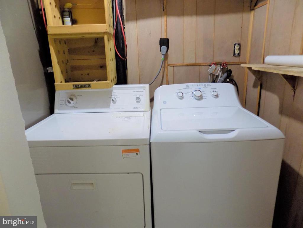 Laundry room with a white washer and dryer beneath wooden shelving.