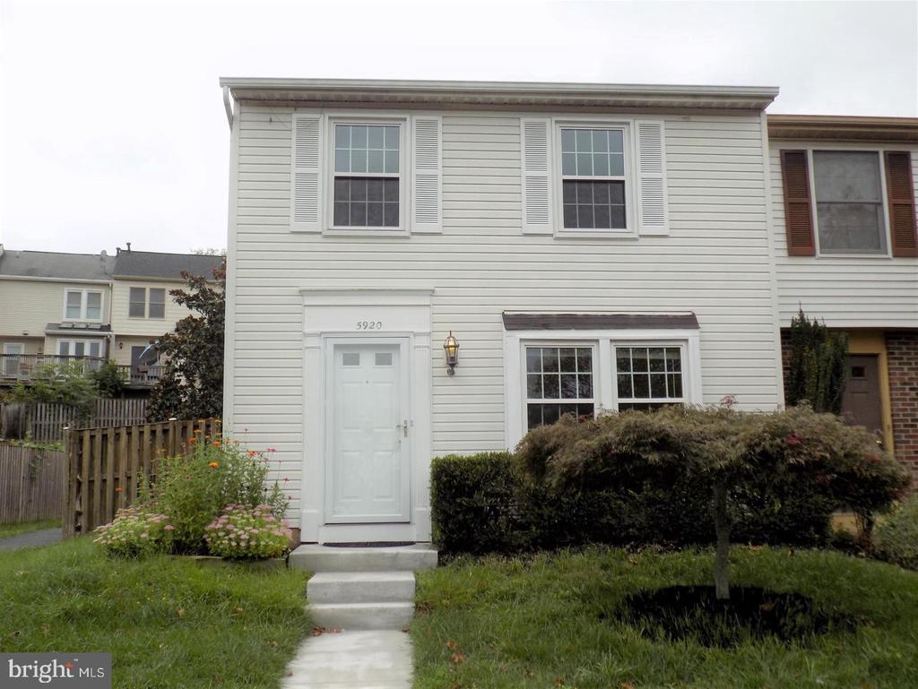 White-sided townhouse with a white front door, upper windows, shrubs, and a short walkway.