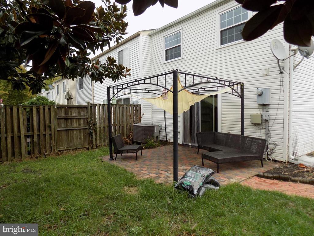 White-sided home’s backyard with a fenced brick patio, metal pergola, and outdoor seating.