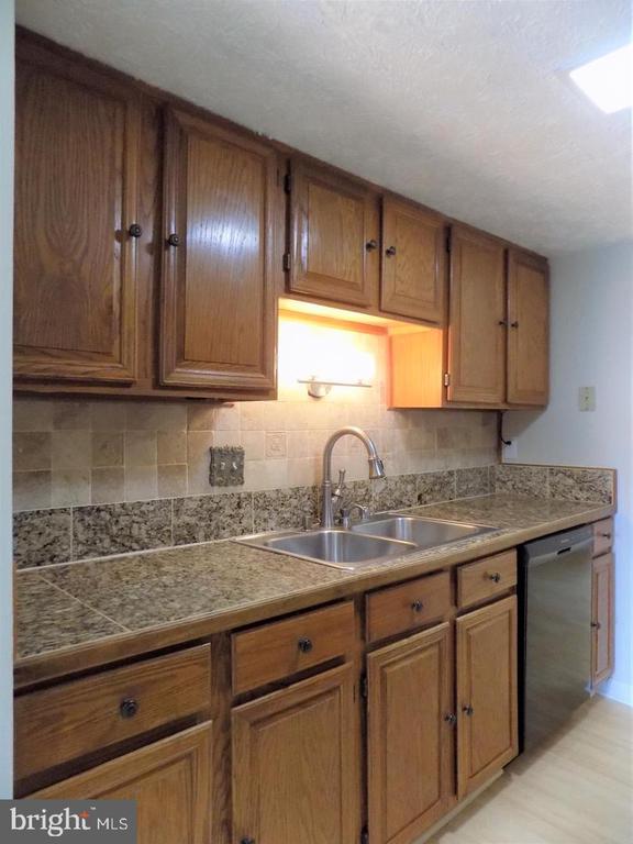 Kitchen with oak cabinets, granite counters, stainless sink, and tiled backsplash.