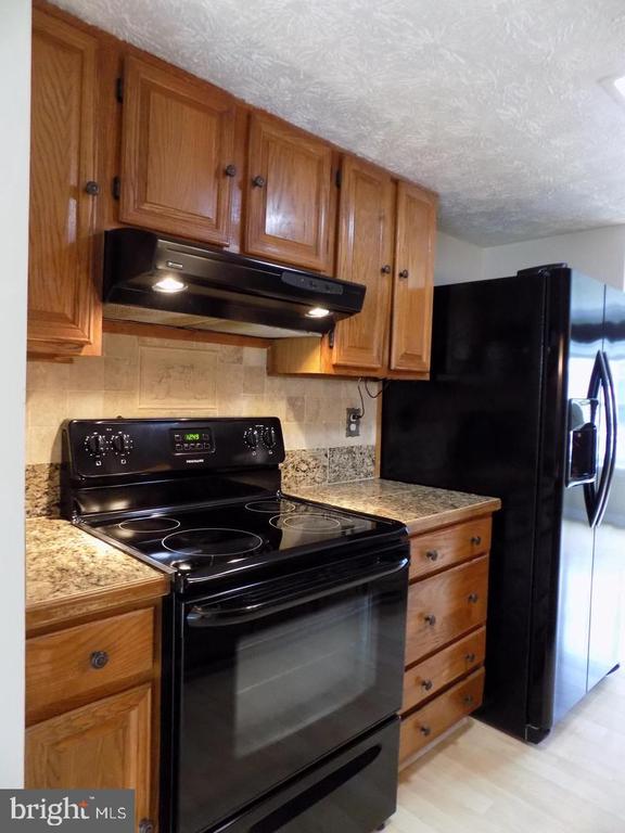 Kitchen with wood cabinets, speckled countertops, a black electric range, and a side-by-side refrigerator.