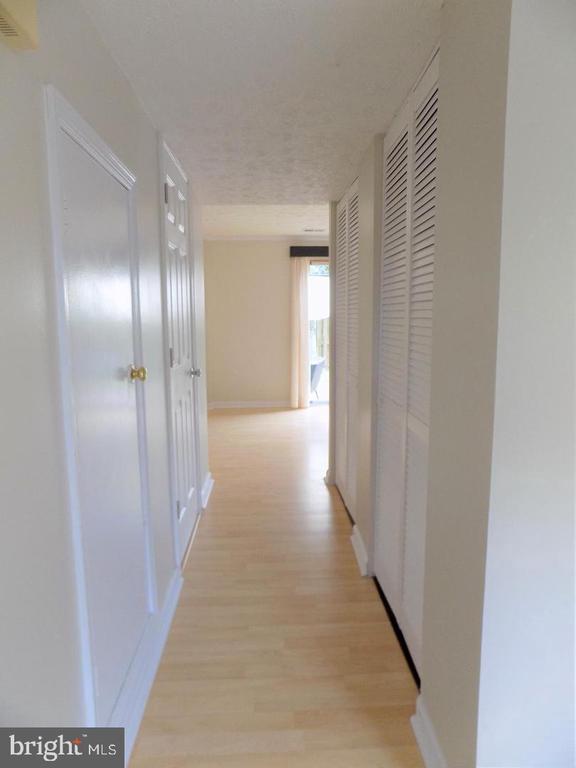 Empty hallway with light wood floors, white doors, and louvered closet doors.