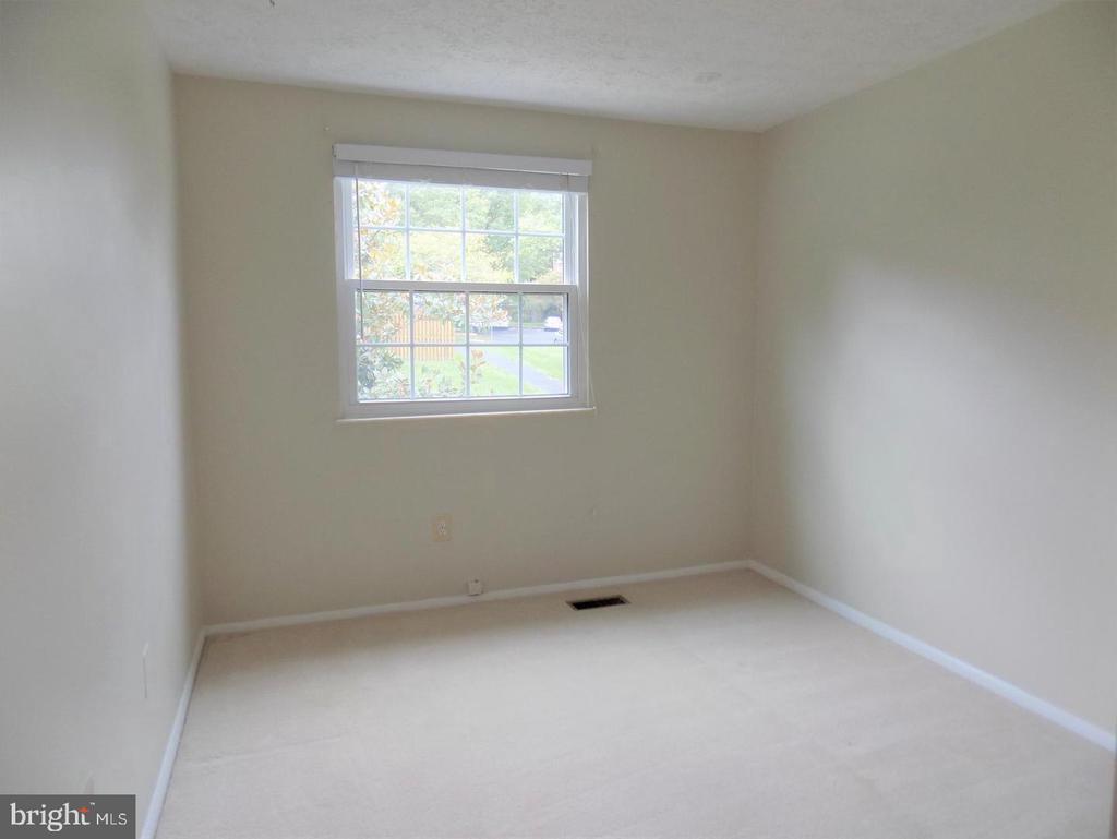 Empty carpeted bedroom with pale walls and a double-hung window overlooking greenery.