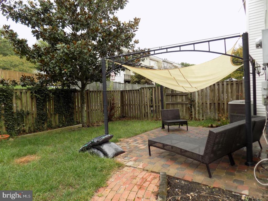 Fenced backyard patio with brick pavers, outdoor seating, and a cream shade canopy.