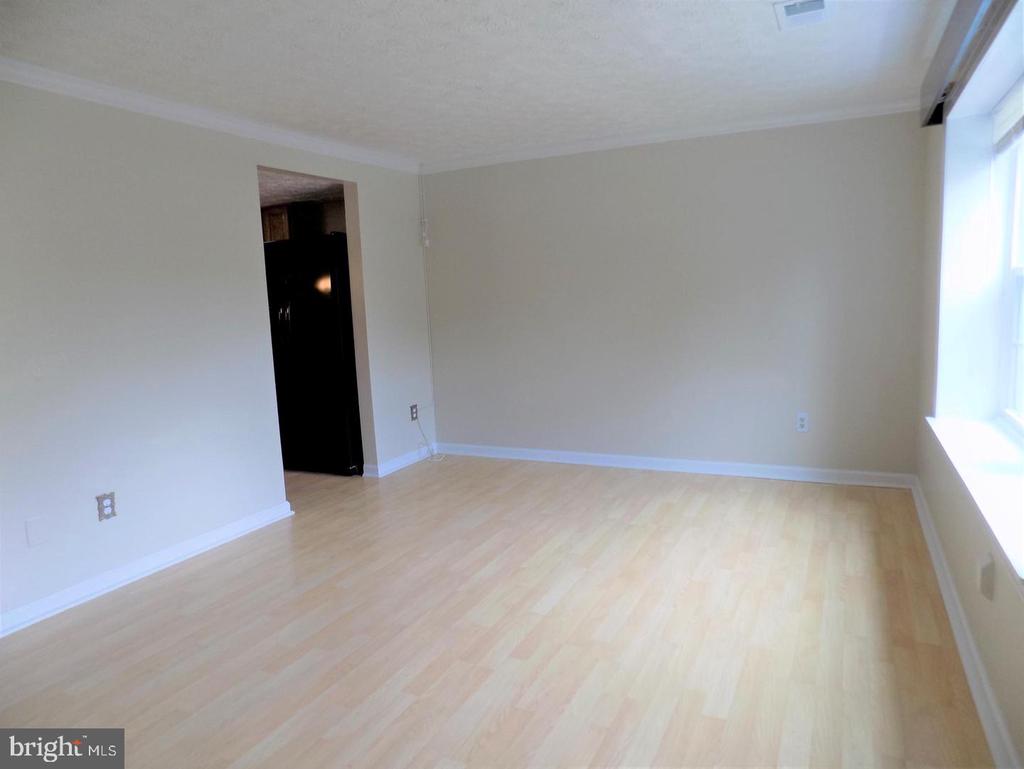 Vacant living room with pale wood floors and a large window.