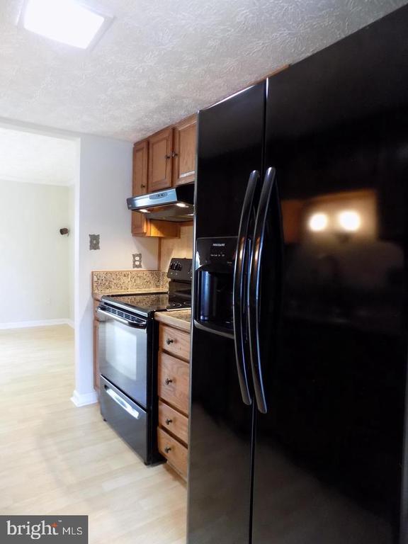 Kitchen with black refrigerator and range, wood cabinets, and light stone-patterned counters.