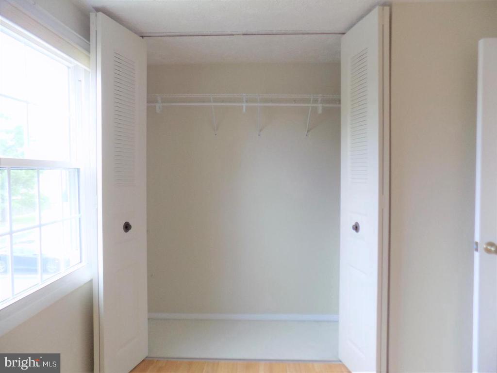 Empty walk-in closet with open louvered doors, a wire shelf and rod, and a window beside it.