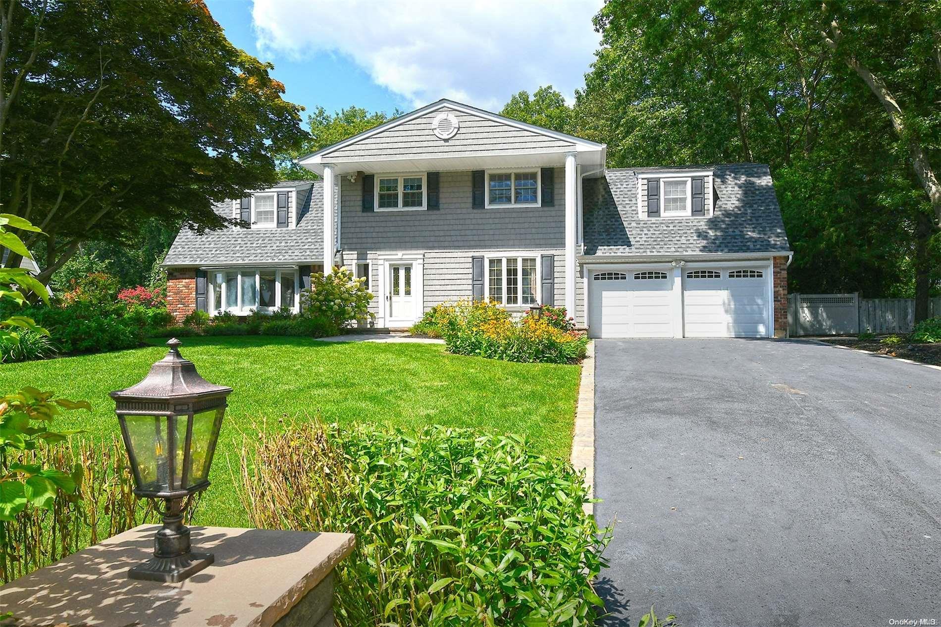 Gray two-story shingle house with dormers, double garage, landscaped lawn, and wide driveway.