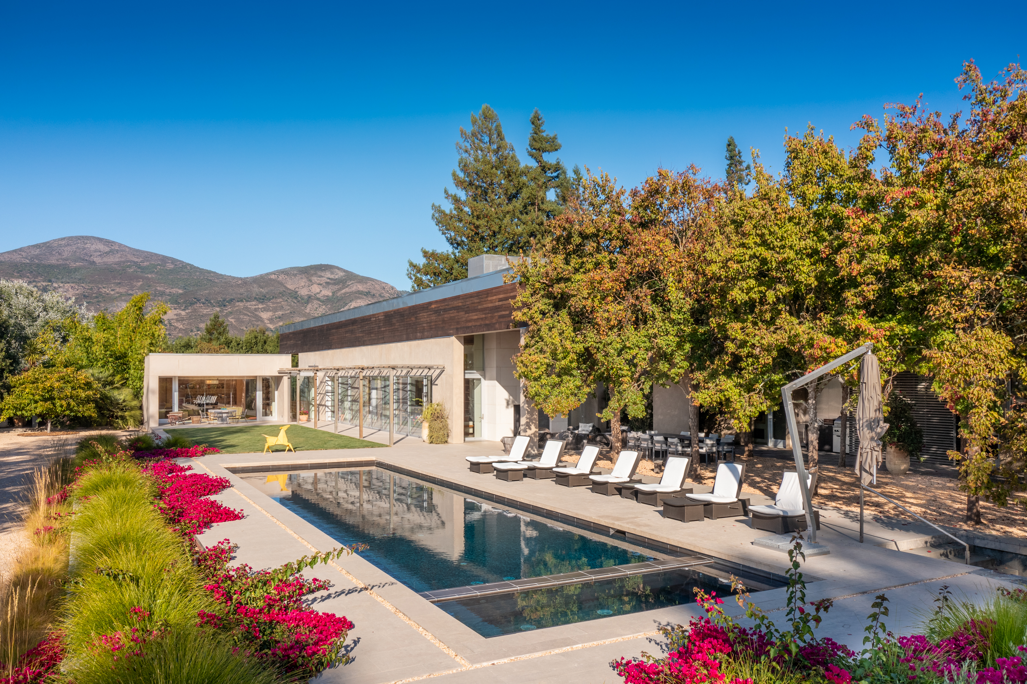 Modern home and long pool framed by autumn trees, with hills in the background.