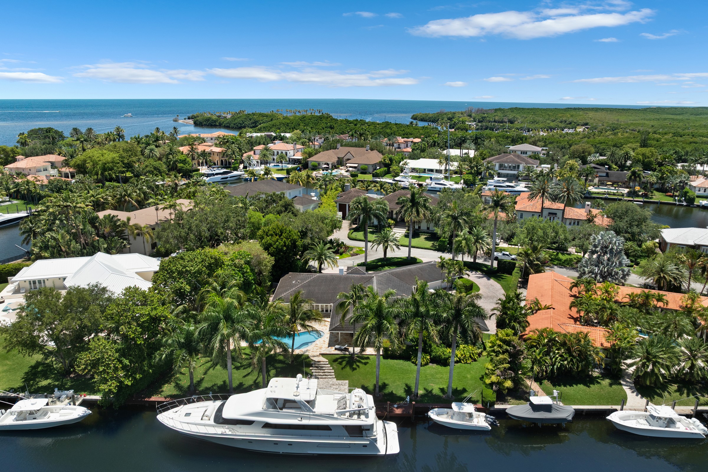 Aerial view of palm-lined waterfront homes, docks, and boats beside the open sea.