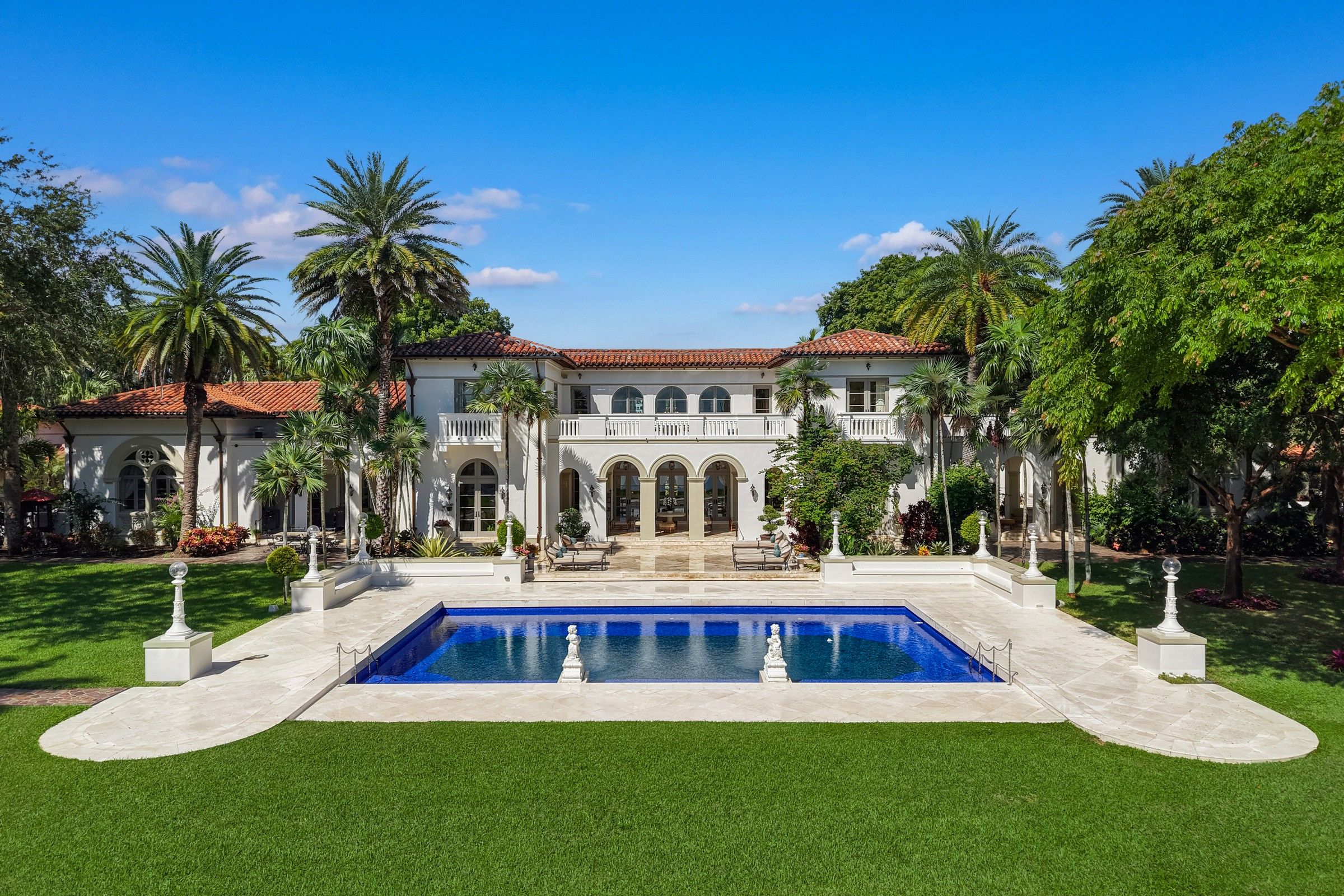 Mediterranean-style estate with a red tile roof, palm-lined lawn, and rectangular pool.