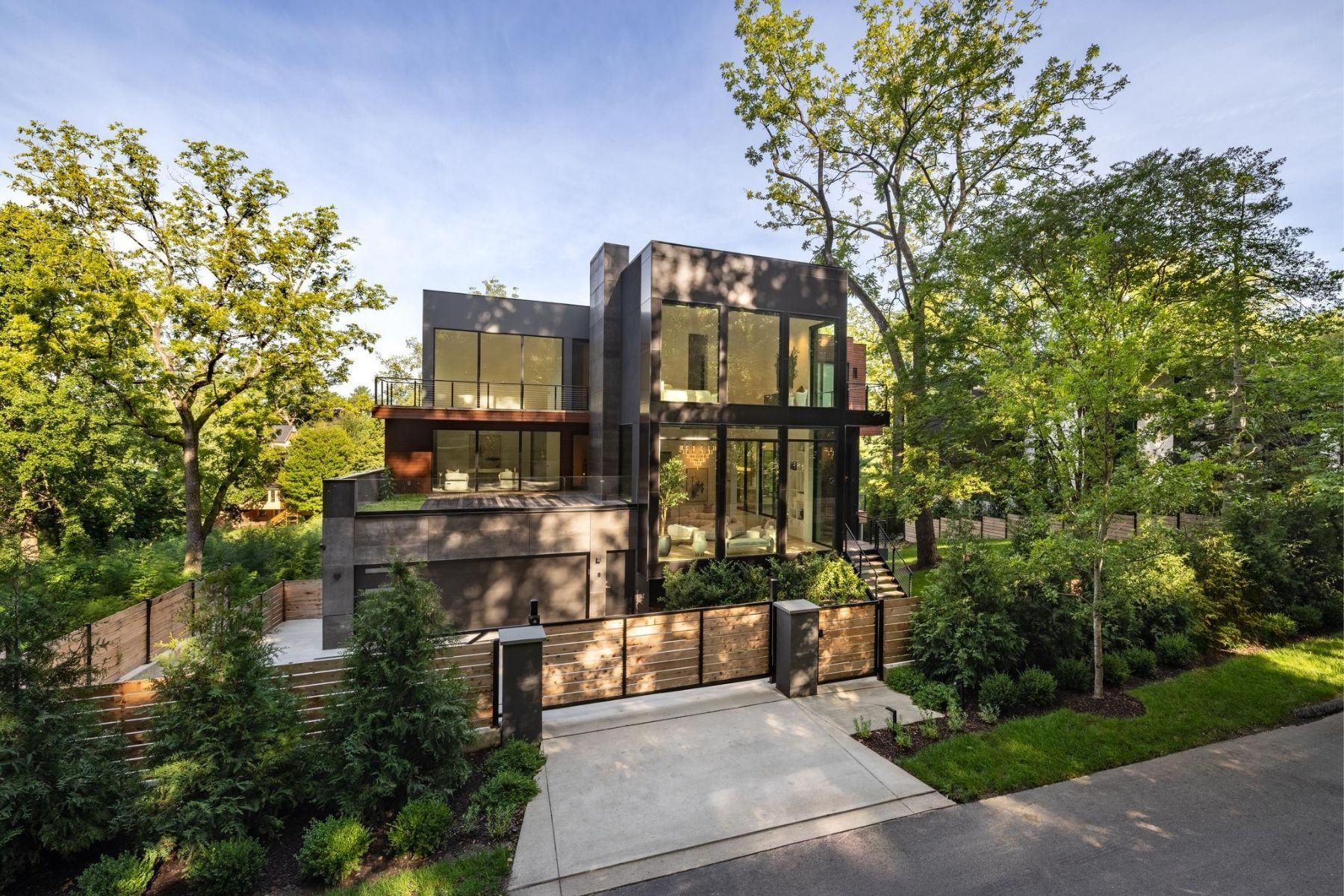Modern home with expansive glass windows, dark stone exterior, and landscaped wooded grounds.