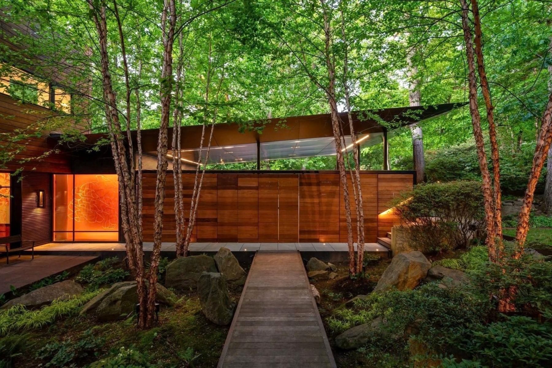 Modern wood-clad home among trees, approached by a boardwalk.