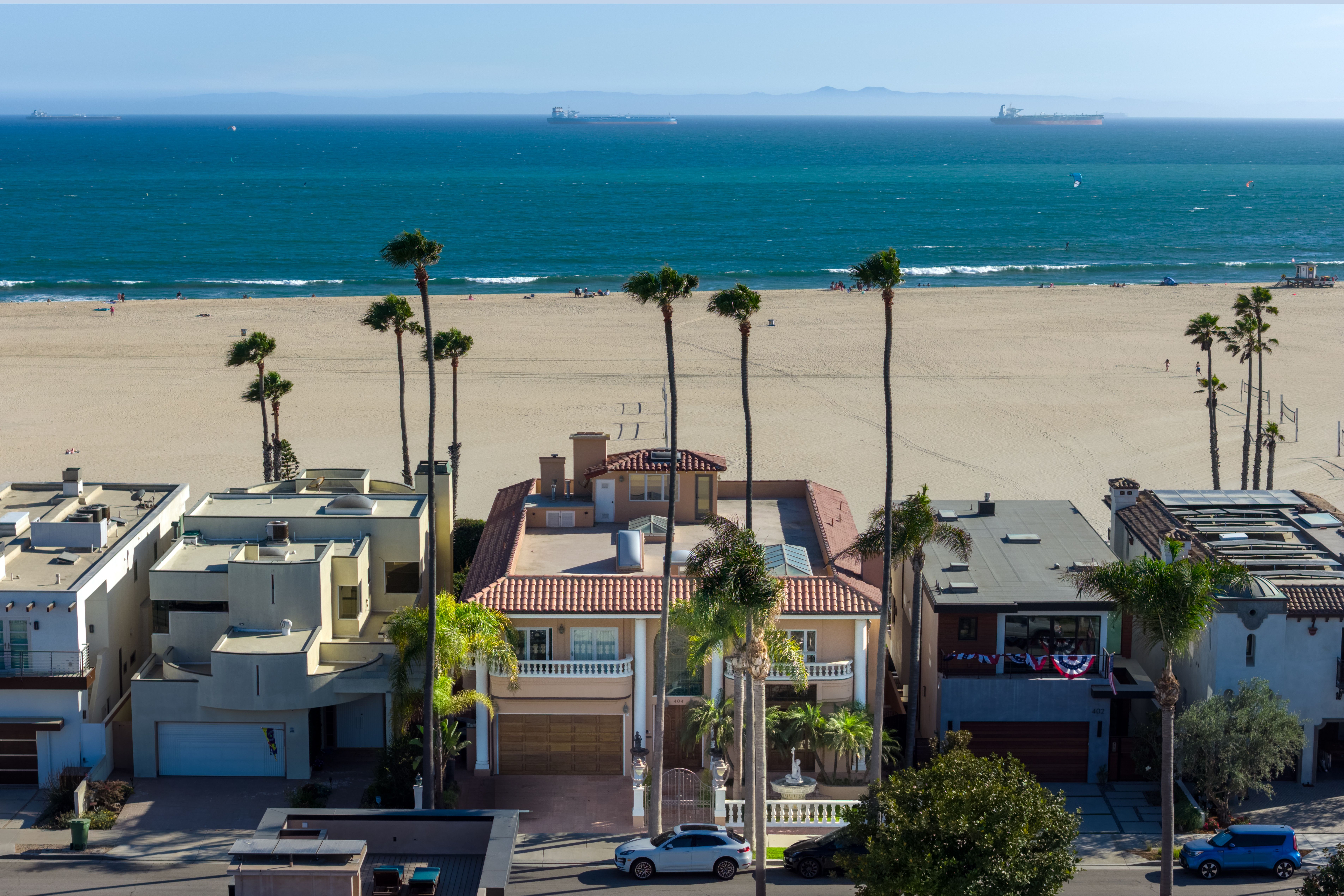 Beachfront home with a tiled roof and balcony, palm trees, and a sandy beach beyond.