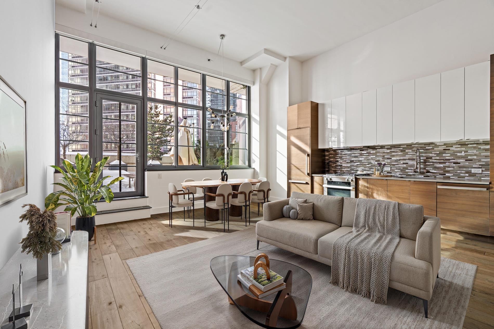 Open-plan living room and kitchen with high ceilings, large industrial-style windows, and a gray sofa.
