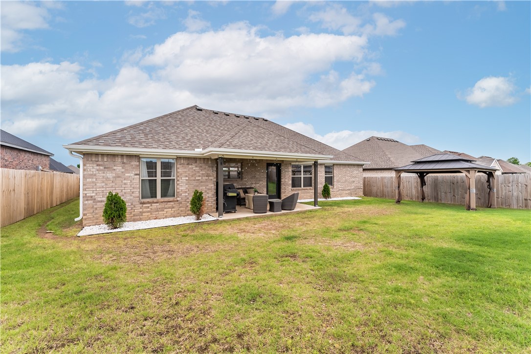 Brick home with a covered patio and outdoor seating overlooking a wide fenced lawn.