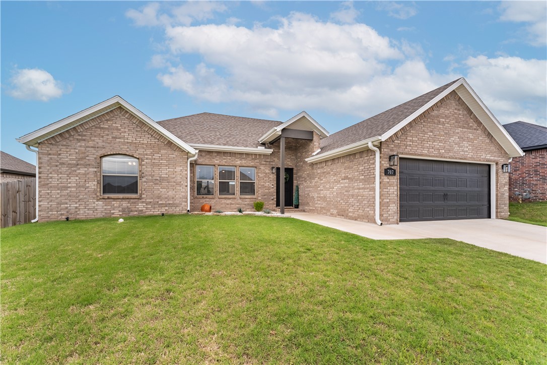 Tan brick home with a dark double garage, covered entry, and broad front lawn.