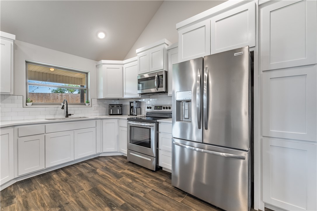 Kitchen with white cabinets, stainless steel appliances, and dark wood-look flooring.