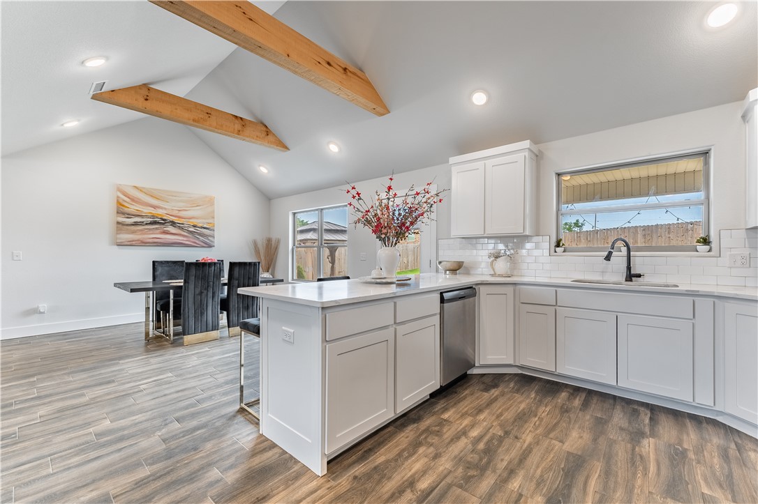 Open kitchen with a large white island, exposed wood ceiling beams, and dining area.