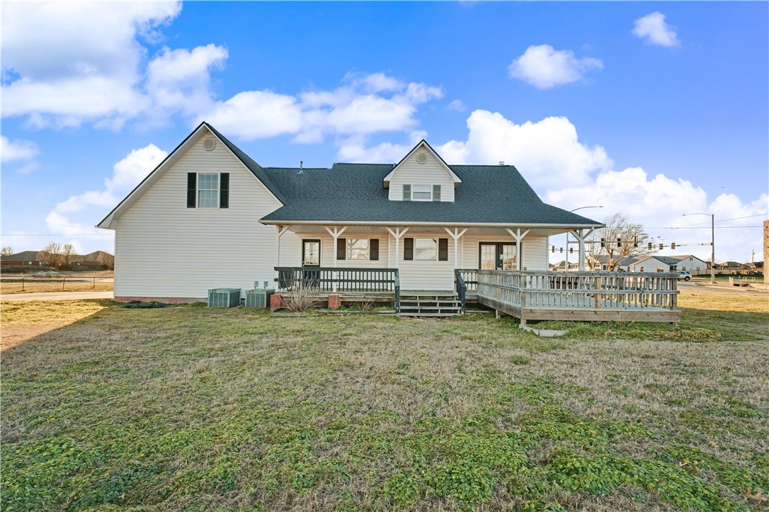 White-sided house with a covered porch and raised wooden deck overlooking a broad lawn.