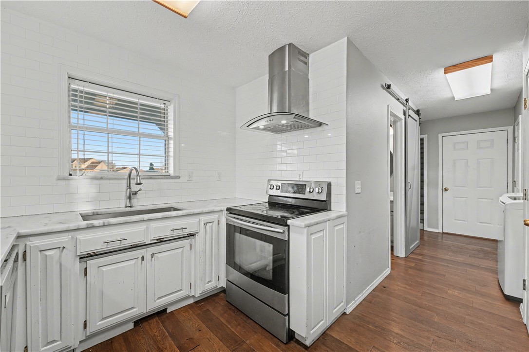 Kitchen with white cabinets and tile, stainless steel range, and a sink beneath a window.