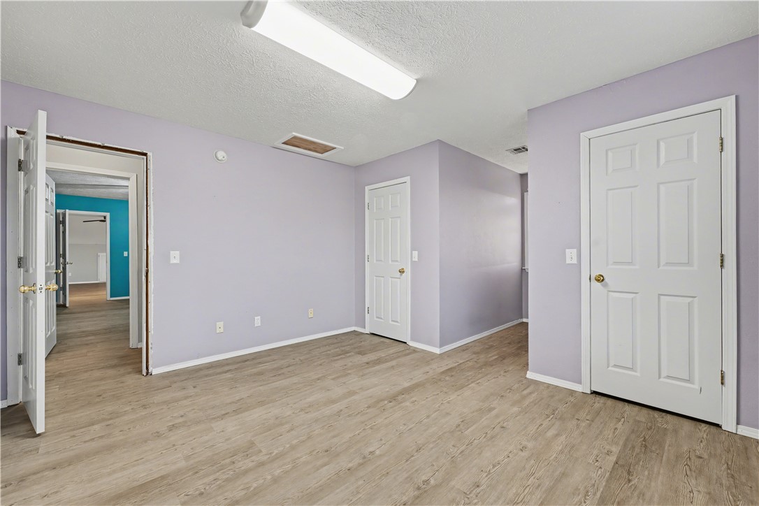 Vacant room with pale lavender walls, wood-look flooring, and three white doors.