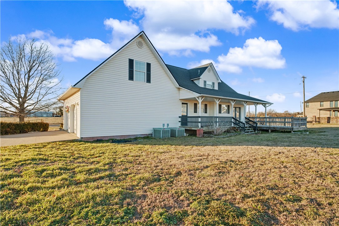 White-sided house with gabled roofs, covered porch, and long wooden deck beside a grassy yard.