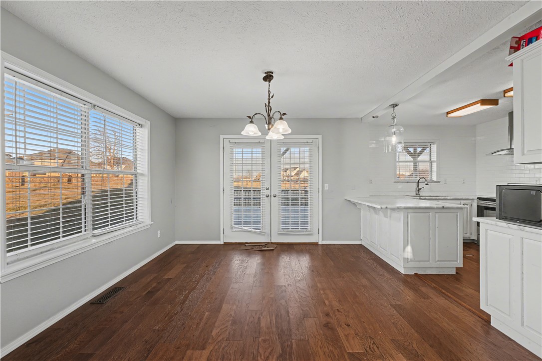 Unfurnished dining area with dark hardwood floors, a chandelier, and glazed double doors beside a white kitchen.