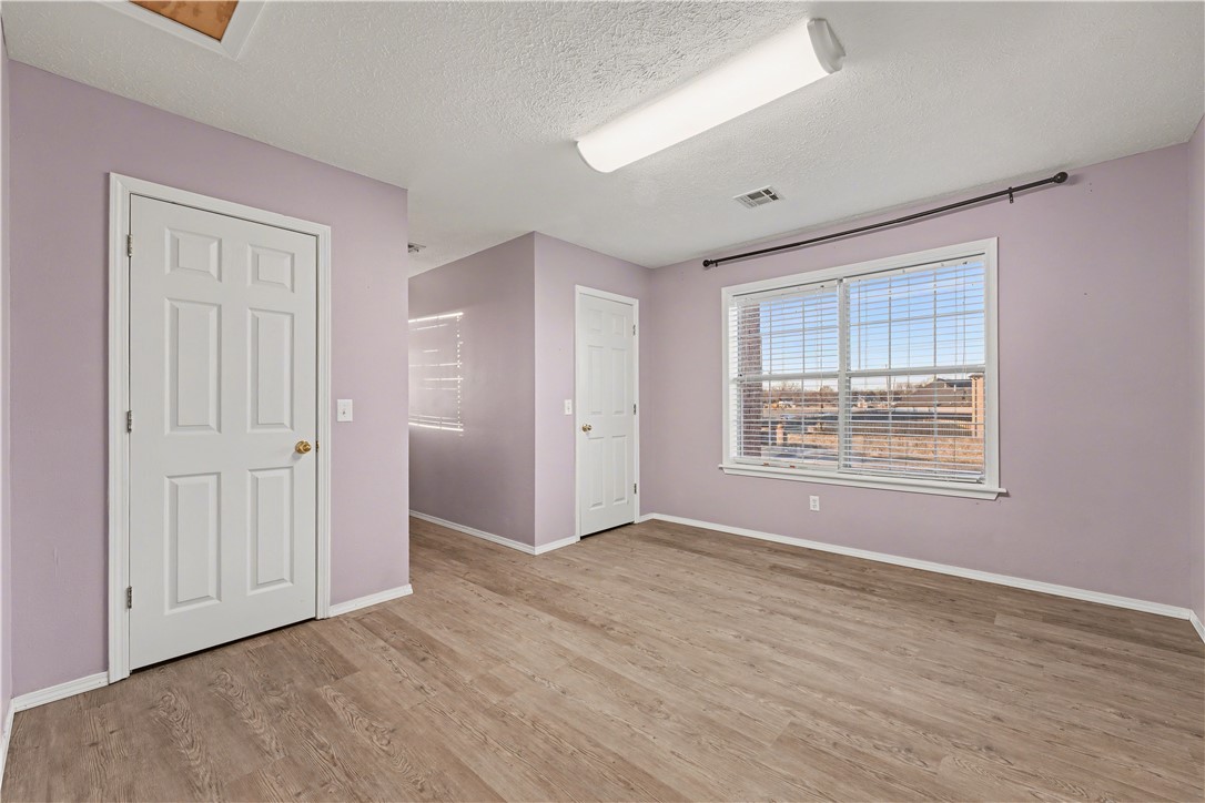 Empty room with lavender walls, wood-look flooring, two doors, and a large window.
