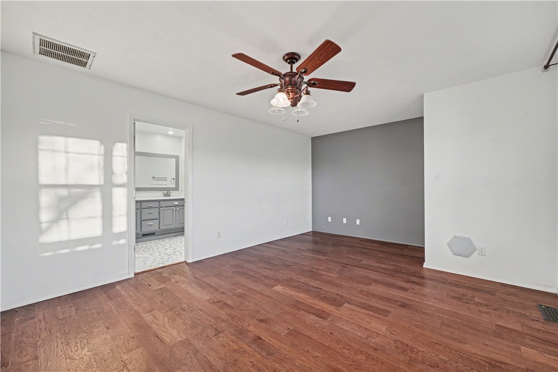 Unfurnished room with hardwood floors, a gray accent wall, and a ceiling fan.