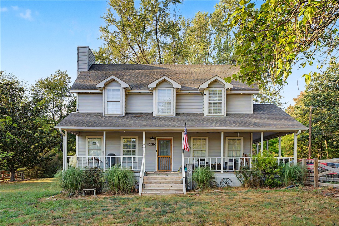 Gray two-story home with three dormers, a wide front porch, and an American flag.