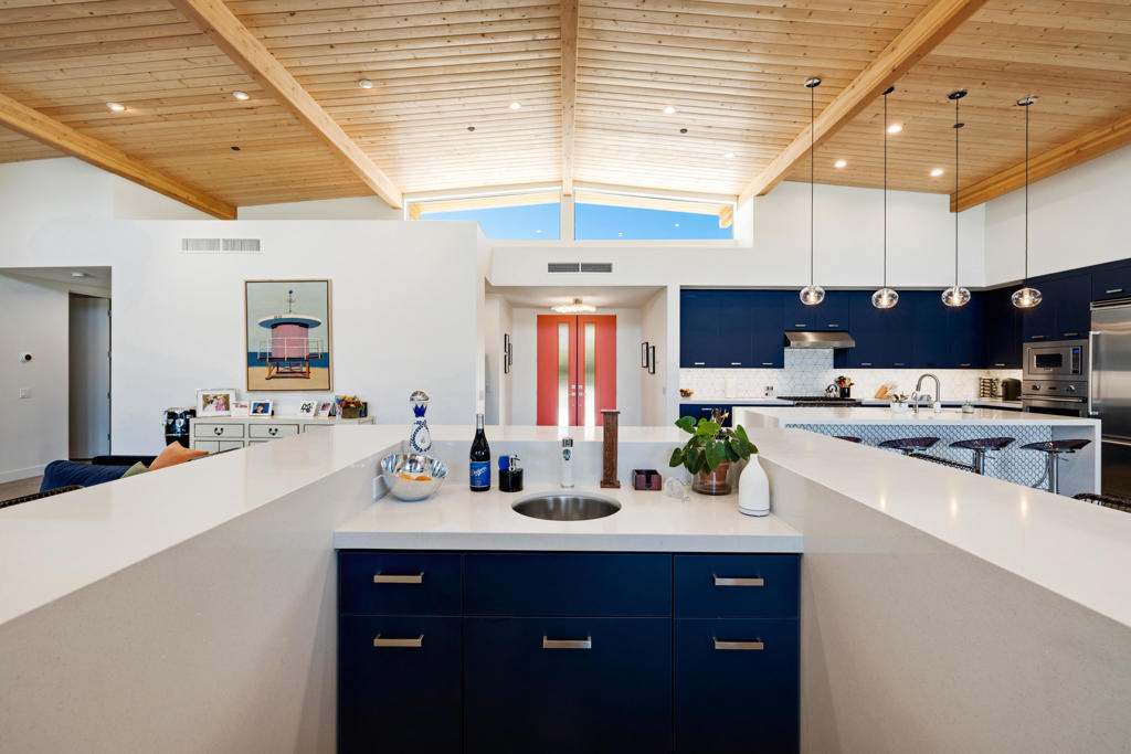 Open-plan kitchen with navy cabinets, a large white island, and a vaulted wood-beam ceiling.