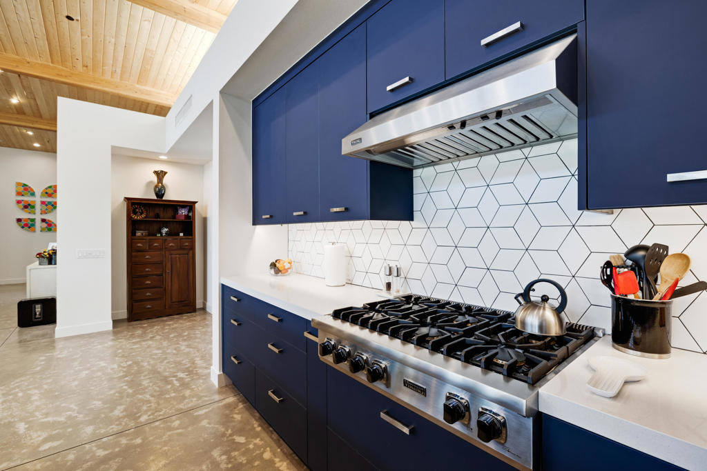 Modern kitchen with blue cabinets, geometric tile backsplash, stainless-steel range, and wood-plank ceiling.
