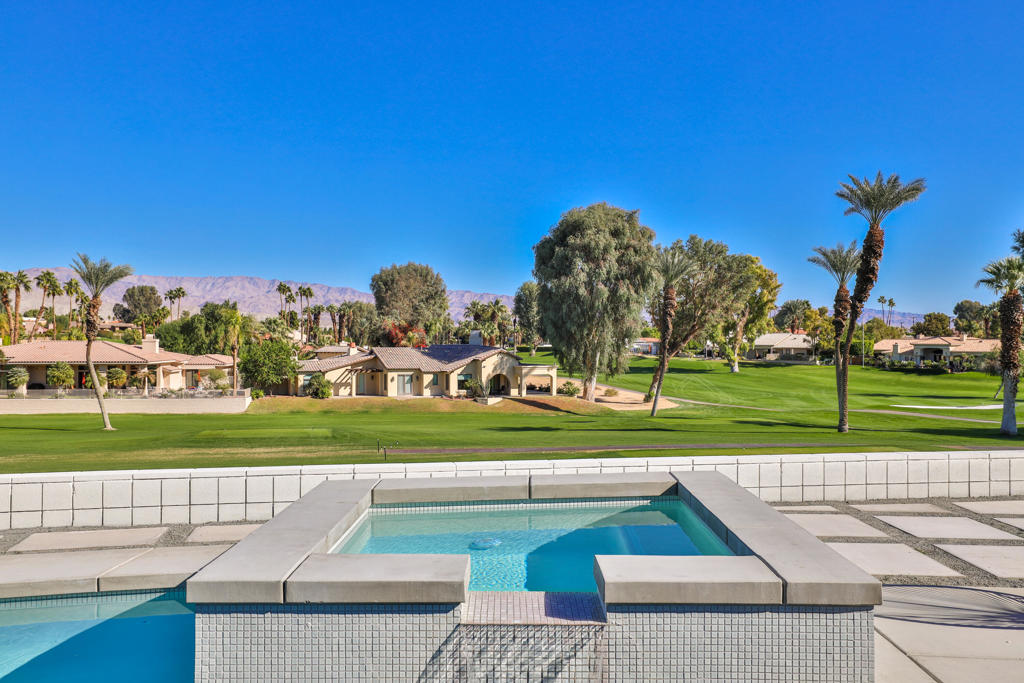 Raised swimming pool overlooks a golf course, with homes and mountains beyond.