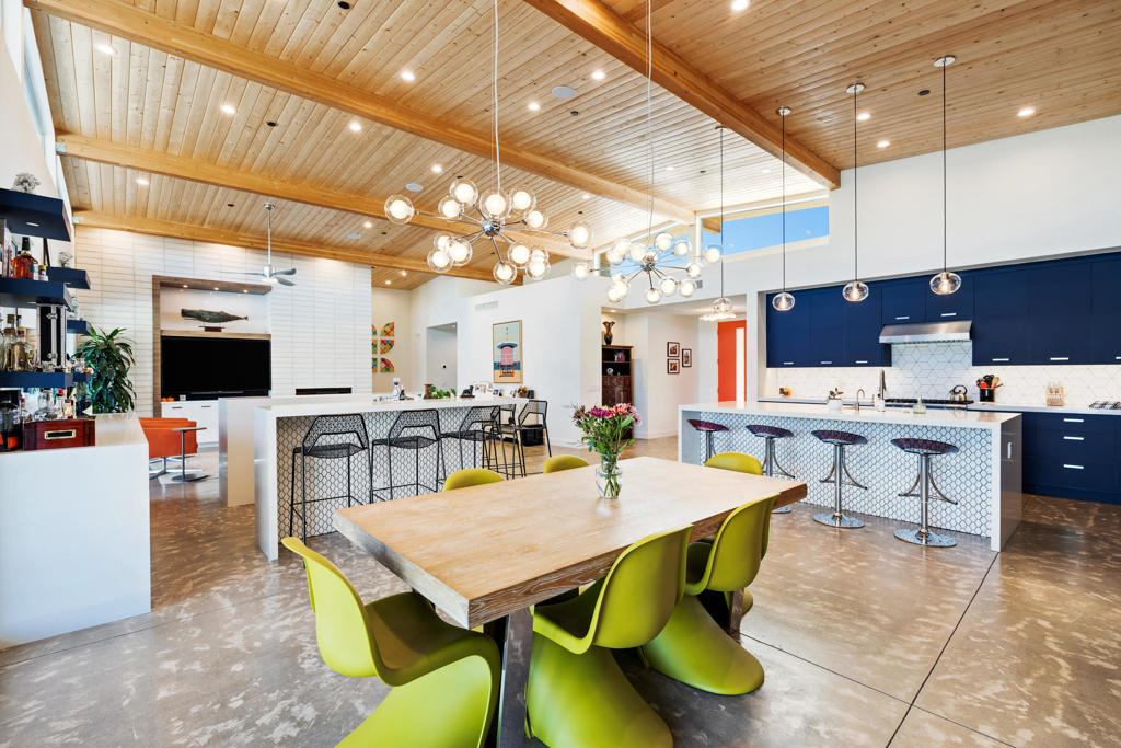 Open-plan kitchen and dining area with navy cabinets, lime-green chairs, and a vaulted wood ceiling.