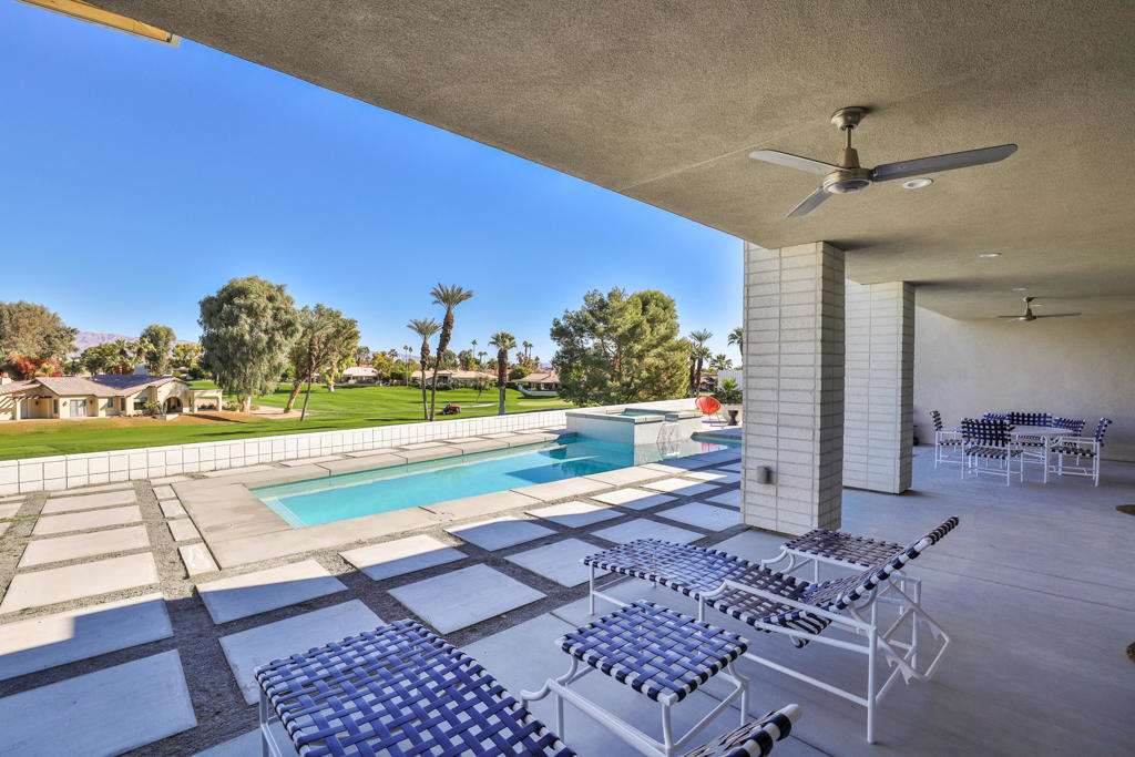 Covered patio with lounge chairs overlooking a swimming pool and manicured golf course.