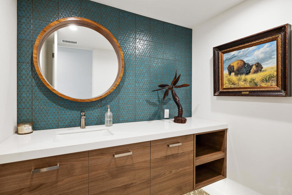 Bathroom vanity with teal geometric tile, a round mirror and walnut cabinets.