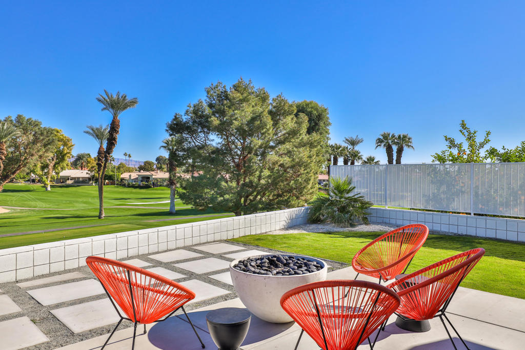 Backyard patio with red chairs and a fire bowl overlooking a golf course.