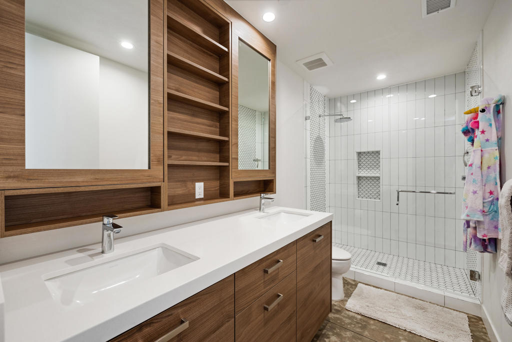 Bathroom with a double-sink wood vanity and a glass-enclosed white-tile shower.