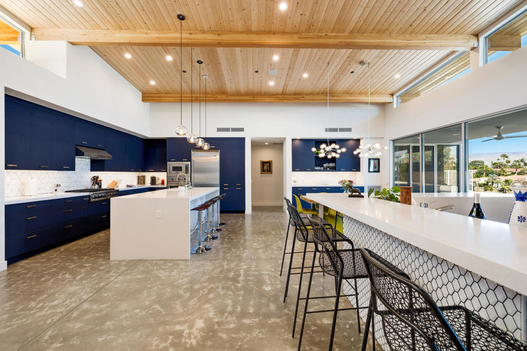 Open-plan kitchen with navy cabinets, a long white island, and a wood-plank ceiling.