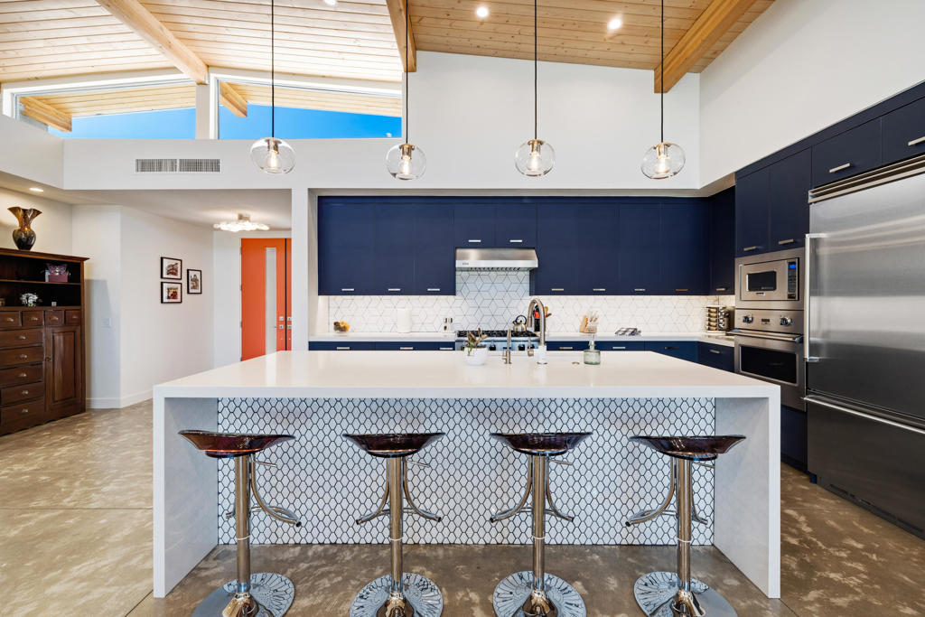 Modern kitchen with navy cabinets, a large island, four bar stools, and a vaulted wood ceiling.