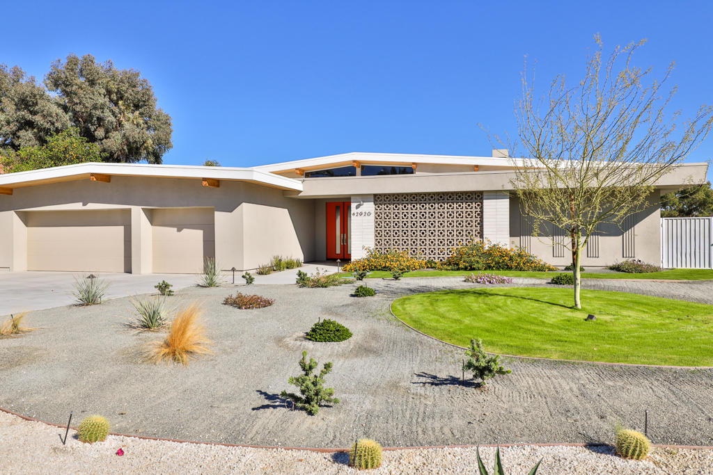 Modern single-story home with red entry door, patterned facade screen, and landscaped gravel-and-lawn yard.